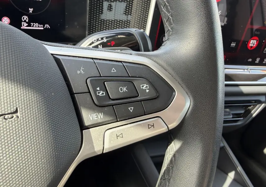 Gros plan sur les commandes multifonctions en cuir du volant côté gauche du Volkswagen Tiguan 2025, avec affichage numérique en arrière-plan.