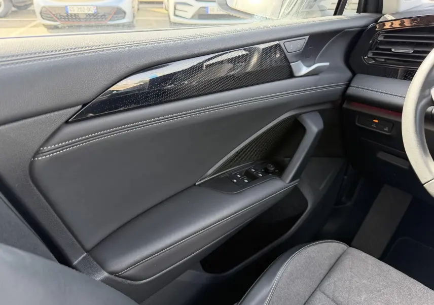 Vue intérieure côté conducteur du Volkswagen Tiguan 2025, montrant la porte en cuir noir avec surpiqûres blanches et commandes électriques.