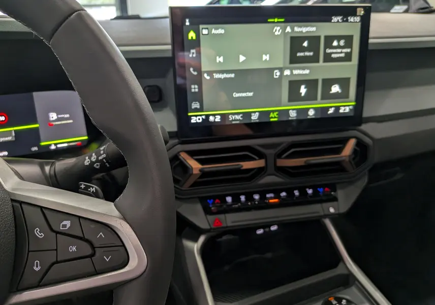 Vue intérieure du tableau de bord du Dacia Bigster Hybrid-G 150 4x4, avec écran tactile central et volant partiel en cuir noir.