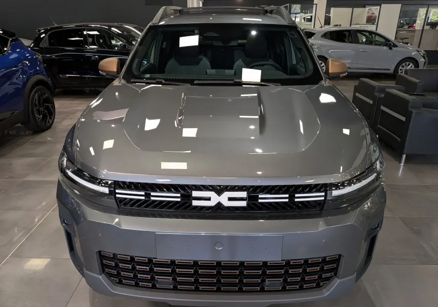 Vue avant du Dacia Bigster Hybrid-G 150 4x4 Extrême gris schiste avec calandre noire et détails cuivrés en showroom.