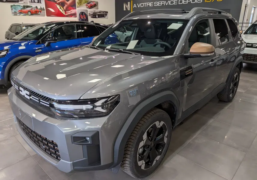 Vue 3/4 avant droite du Dacia Bigster Hybrid-G 150 4x4 gris schiste avec rétroviseurs couleur bronze en showroom.