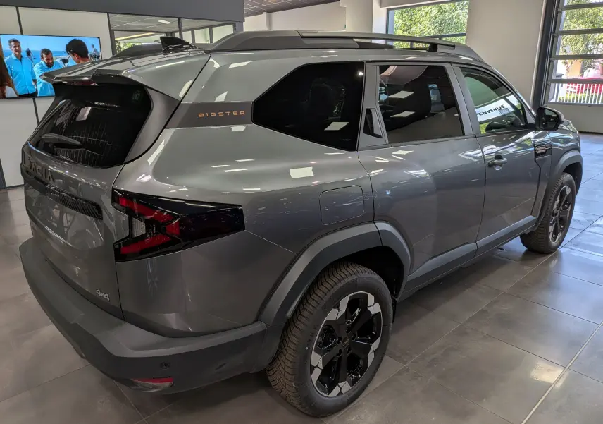 Vue 3/4 arrière droite d'un Dacia Bigster gris schiste avec badge 4x4 et jantes biton noires en showroom.