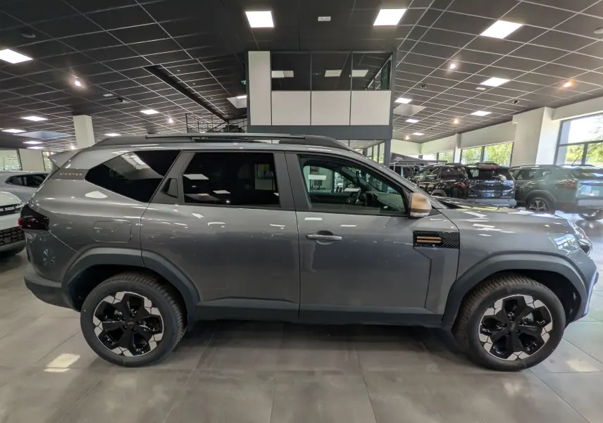 Vue de profil côté gauche du Dacia Bigster Hybrid-G 150 4x4 en gris schiste avec jantes biton noir et toit noir.