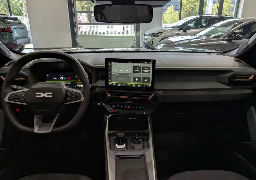 Vue intérieure avant du tableau de bord et volant du Dacia Bigster Hybrid-G 150 4x4 en gris schiste, avec écran tactile central.