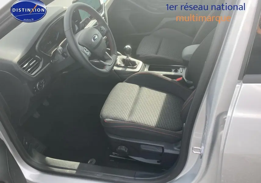 Vue intérieure côté conducteur de la Ford Focus 2025 gris, volant 3 branches avec coutures rouges et boîte manuelle.