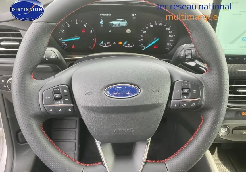 Vue rapprochée du volant perforé noir avec coutures rouges et tableau de bord numérique de la Ford Focus gris 2025.