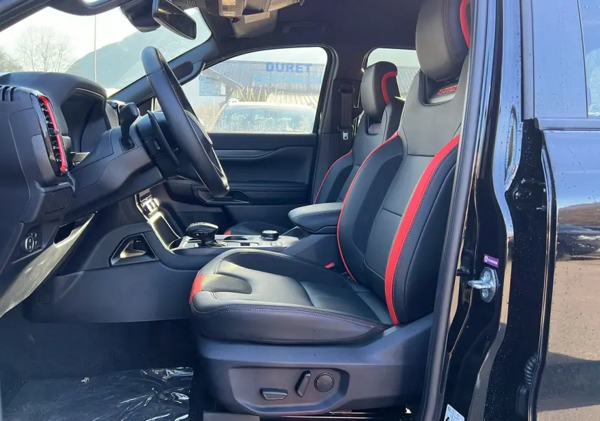 Intérieur côté conducteur du Ford Ranger Raptor 2025 noir, sièges sport cuir noirs avec surpiqûres rouges et volant multifonctions.