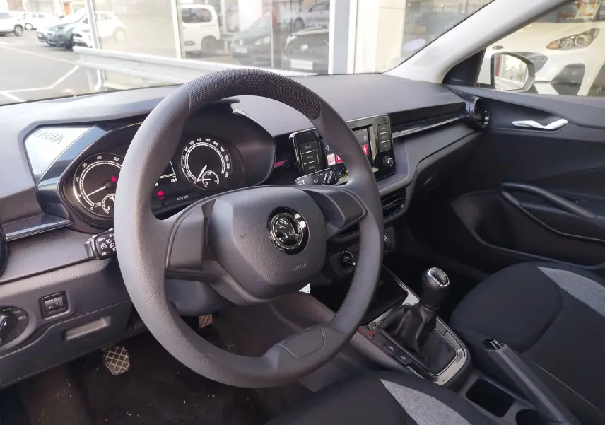 Vue intérieure côté conducteur de la Skoda Fabia 2022, tableau de bord noir avec volant et levier de vitesses manuelle visibles.