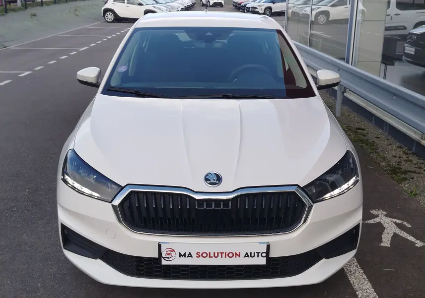 Vue avant d'une Skoda Fabia blanche Lune 2022 avec calandre noire et phares LED allumés sur parking extérieur.