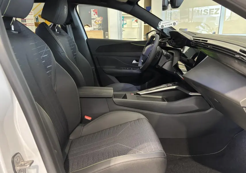 Vue intérieure côté conducteur de la Peugeot 308 Hybrid 2026 avec sellerie noire et surpiqûres vert Adamite.