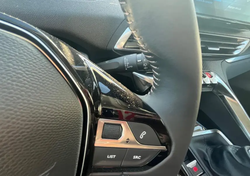 Gros plan sur le volant et la console centrale du Peugeot 3008 2023, mettant en valeur les commandes intégrées et la finition noire.