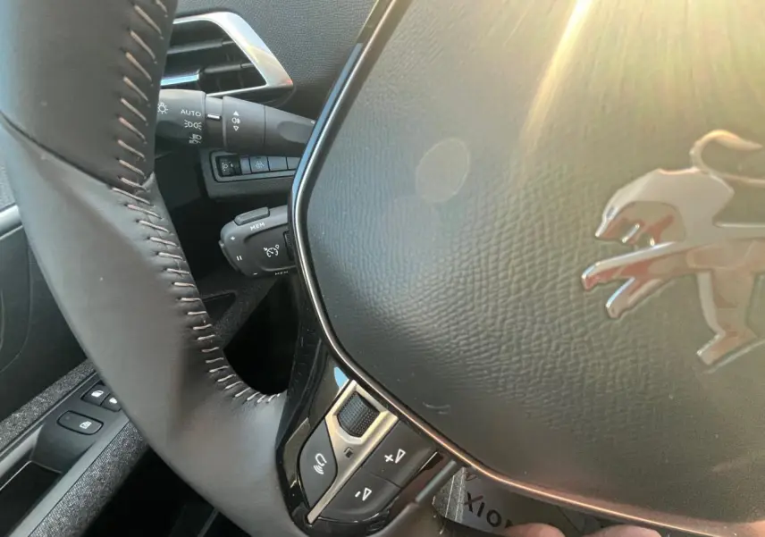 Gros plan sur le volant noir de la Peugeot 3008 2023, avec logo lion et commandes intégrées, lumière naturelle.