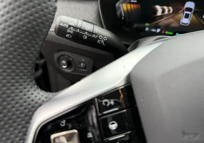 Gros plan sur la manette de commandes d’éclairage et clignotants côté gauche du volant perforé dans l’habitacle noir du MG ZS 2026.