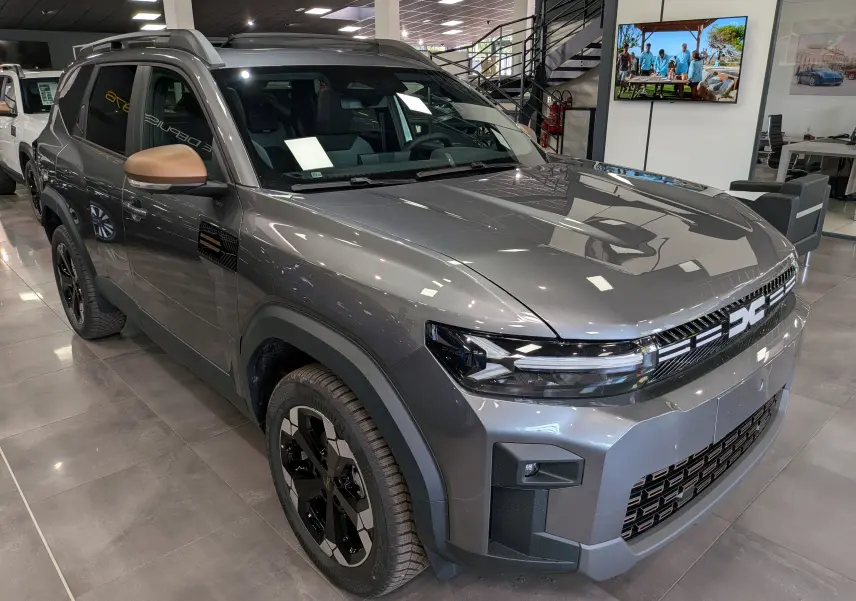 SUV Dacia Bigster Hybrid-G 150 4x4 gris schiste vu en 3/4 avant droit avec rétroviseurs bronze et jantes noires.