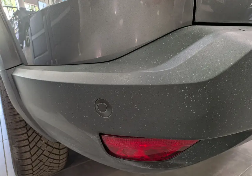 Gros plan sur le pare-chocs arrière gris schiste du Dacia Bigster Hybrid-G 150 4x4, avec feu rouge et capteur de recul visible.