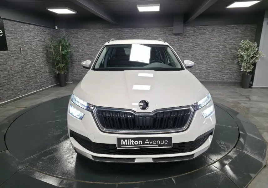 Vue avant d'un Skoda Kamiq blanc avec calandre noire et feux LED allumés dans un showroom.
