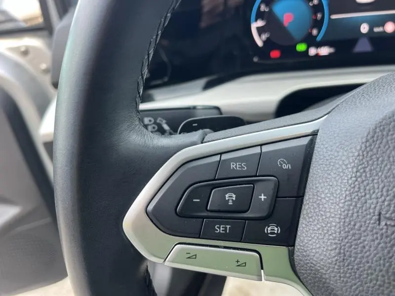 Gros plan sur les commandes multifonctions du volant cuir d'une Volkswagen Golf 1.5 eTSI argentée, tableau de bord digital visible.