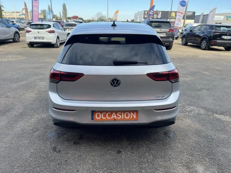 Vue arrière d'une Volkswagen Golf 1.5 eTSI en Reflet d'Argent métallisée avec vitres arrière teintées sur parking.