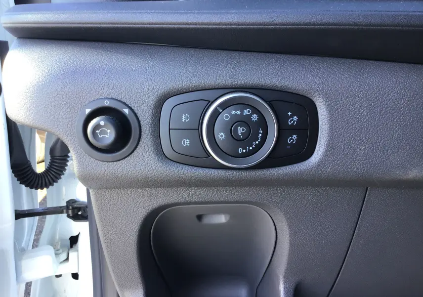 Gros plan sur les commandes d'éclairage et réglage des rétroviseurs côté gauche d'un Ford Transit blanc 2024.