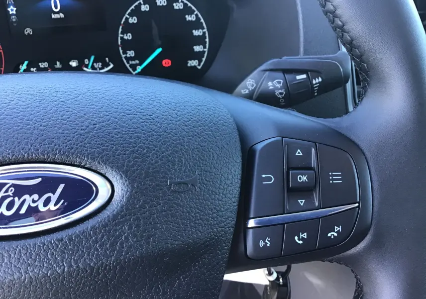 Gros plan sur le volant noir du Ford Transit Châssis Cabine 2024 avec commandes multifonctions et tableau de bord partiel.