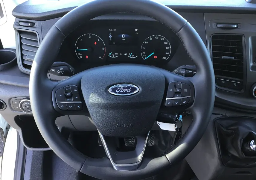 Vue rapprochée du volant multifonction noir du Ford Transit Châssis Cabine blanc, avec tableau de bord digital visible.