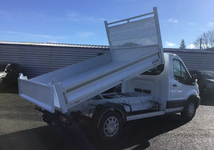 Vue 3/4 arrière droite d'un Ford Transit blanc avec benne basculante levée sur un sol asphalté.