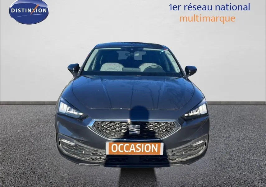 Vue frontale d'une SEAT Leon gris magnétique métal 2025 avec calandre hexagonale et phares LED allumés.