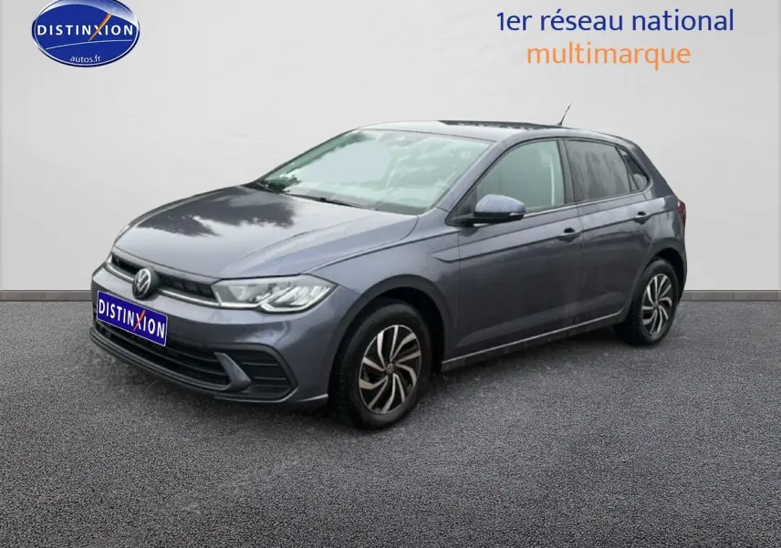 Volkswagen Polo gris cendre vue 3/4 avant droit sur sol gris avec calandre noire et jantes alliage.