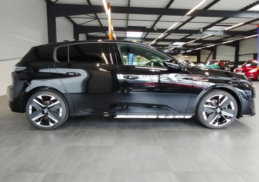 Profil droit d'une Peugeot 308 noire métallisée, avec jantes alliage bi-tons et vitres surteintées en intérieur showroom.
