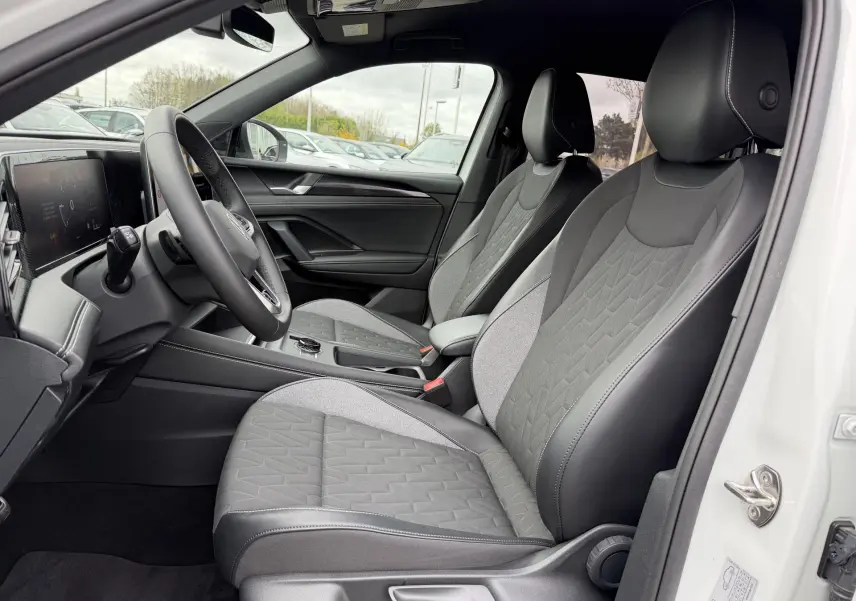 Vue intérieure côté conducteur du Volkswagen Tiguan blanc 2025, sièges avant en tissu et cuir, volant multifonction cuir.