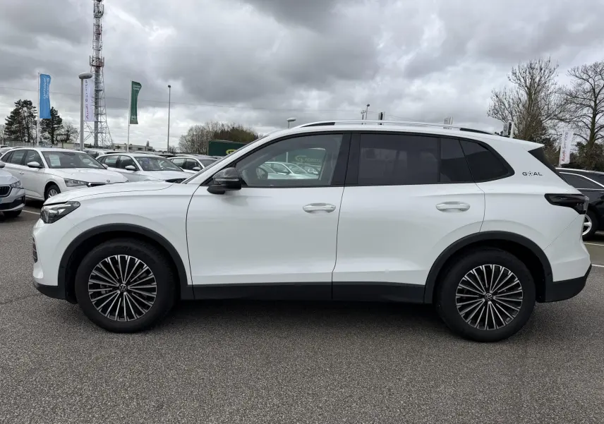 Vue de profil côté gauche d'un Volkswagen Tiguan blanc 2025 avec jantes noires et vitres arrière teintées.