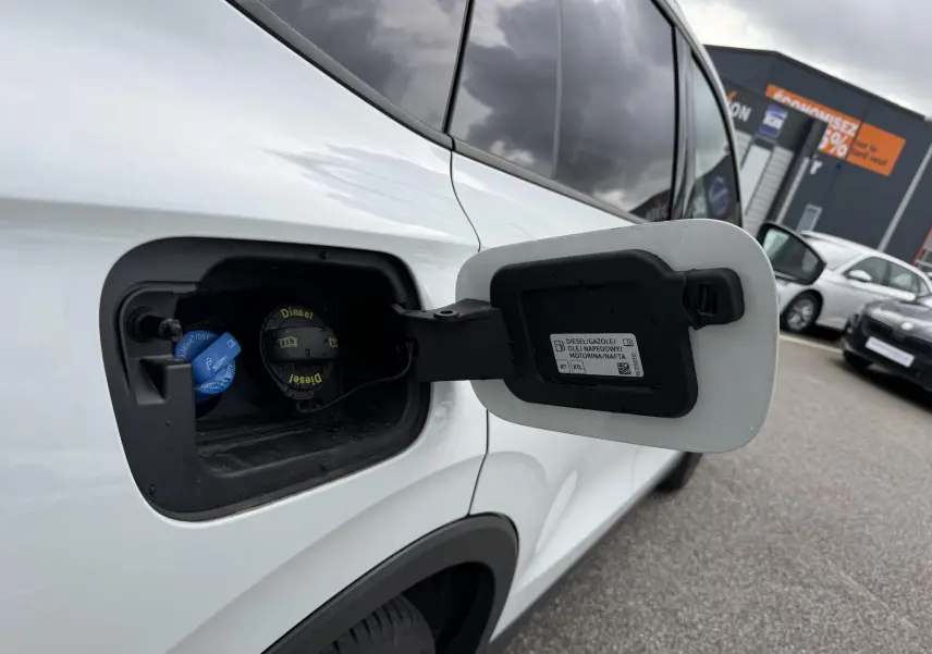 Vue rapprochée de la trappe à carburant ouverte côté gauche d’un Volkswagen Tiguan blanc avec bouchon diesel visible.
