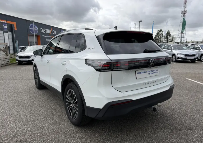 Vue 3/4 arrière droite du Volkswagen Tiguan blanc 2025 avec attelage rabattable et vitres arrière teintées.