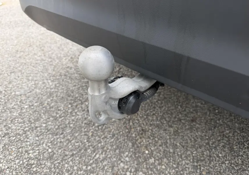 Gros plan sur l'attelage rabattable en métal gris sous le pare-chocs arrière noir d'un Volkswagen Tiguan blanc.