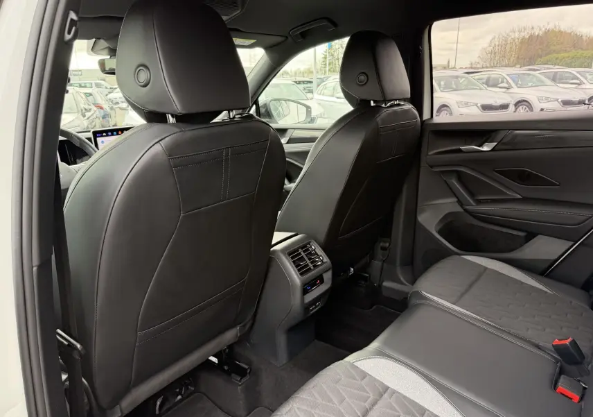 Vue arrière de l'intérieur du Volkswagen Tiguan 2025 blanc, sièges en cuir noir et tissu gris, avec console centrale et aérateurs.