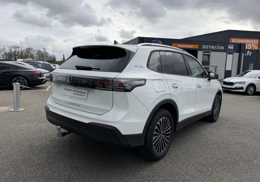 Vue 3/4 arrière droite du Volkswagen Tiguan blanc avec vitres arrière teintées et attelage rabattable visible.