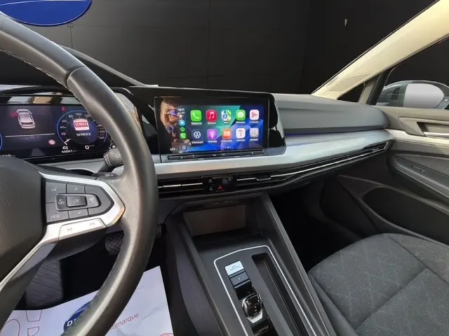 Vue intérieure côté conducteur de la Volkswagen Golf 2023 gris clair, avec écran tactile central et volant multifonctions.