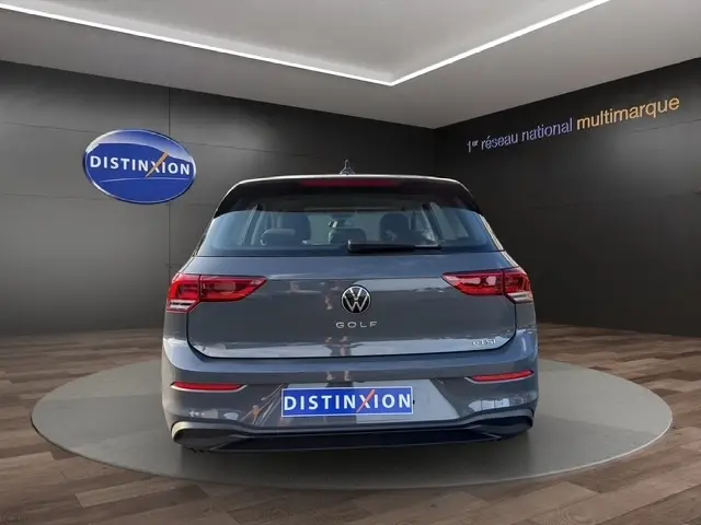 Vue arrière d'une Volkswagen Golf gris clair 2023, avec logo VW et feux LED distinctifs dans un showroom.