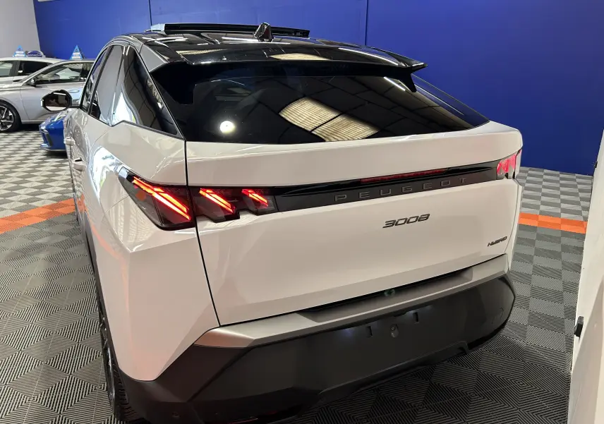 Vue 3/4 arrière droite du Peugeot 3008 blanc Okenite avec feux arrière allumés et toit panoramique noir.