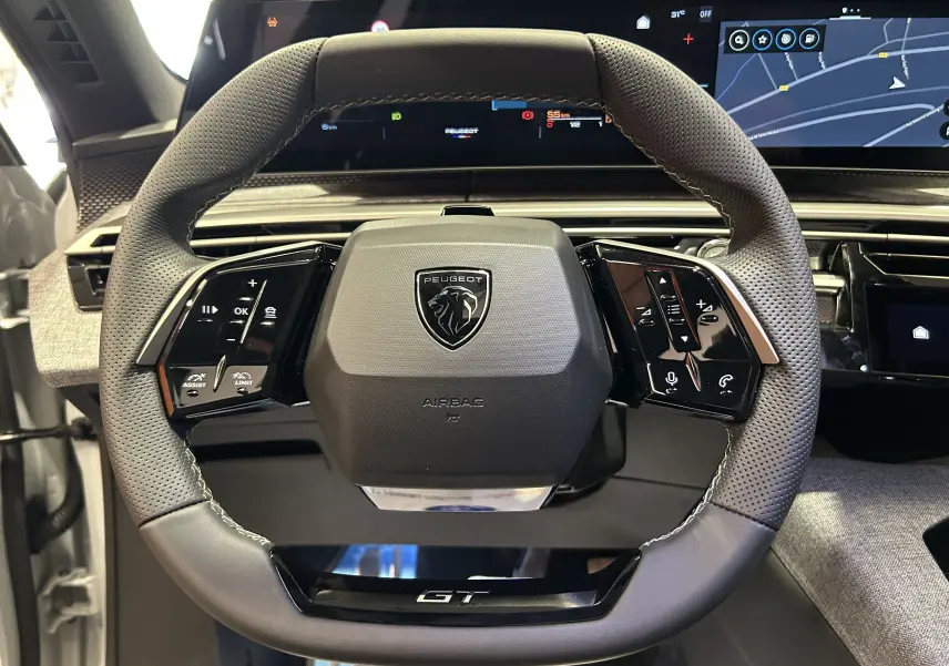 Vue rapprochée du volant cuir perforé noir du Peugeot 3008 III Hybrid GT avec logo lion et commandes intégrées.