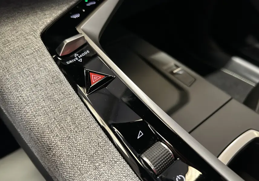 Gros plan sur la console centrale noire brillante du Peugeot 3008 Hybrid 2026 avec bouton triangle rouge de warning.