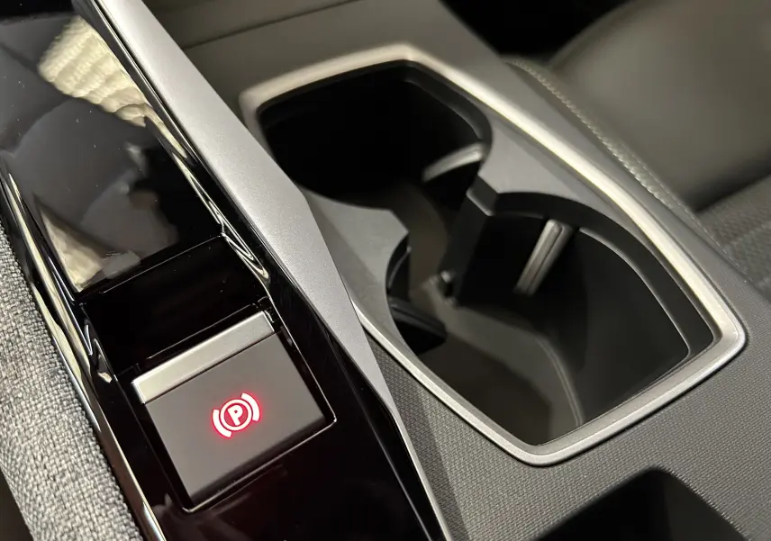 Gros plan sur la console centrale noire et grise du Peugeot 3008 Hybrid, avec bouton de frein à main électronique éclairé en rouge.