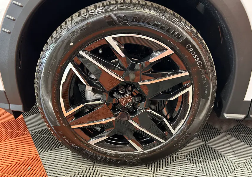 Gros plan sur la roue avant droite du Peugeot 3008 Hybrid blanc Okenite avec jante alliage noire et inserts chromés.