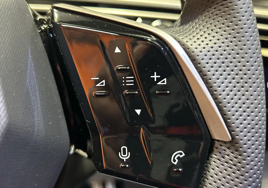Gros plan sur les commandes noires du volant perforé côté gauche du Peugeot 3008 blanc Okenite hybride 2026.