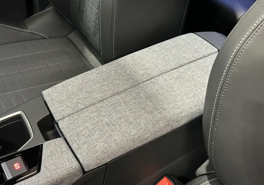 Détail de l'accoudoir central en tissu gris clair et cuir noir dans l'habitacle du Peugeot 3008 Hybrid 2026.