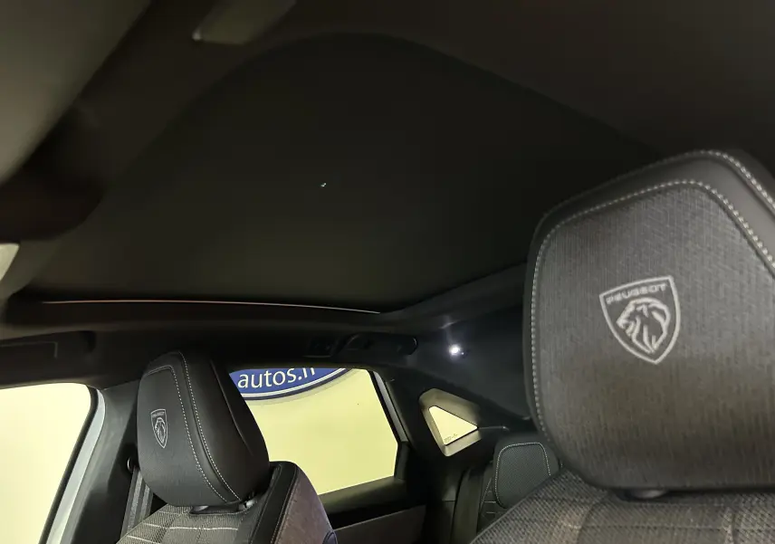 Vue intérieure du Peugeot 3008 Hybrid 2026, montrant les appuis-tête avant avec logo Peugeot brodé et toit ouvrant panoramique noir.