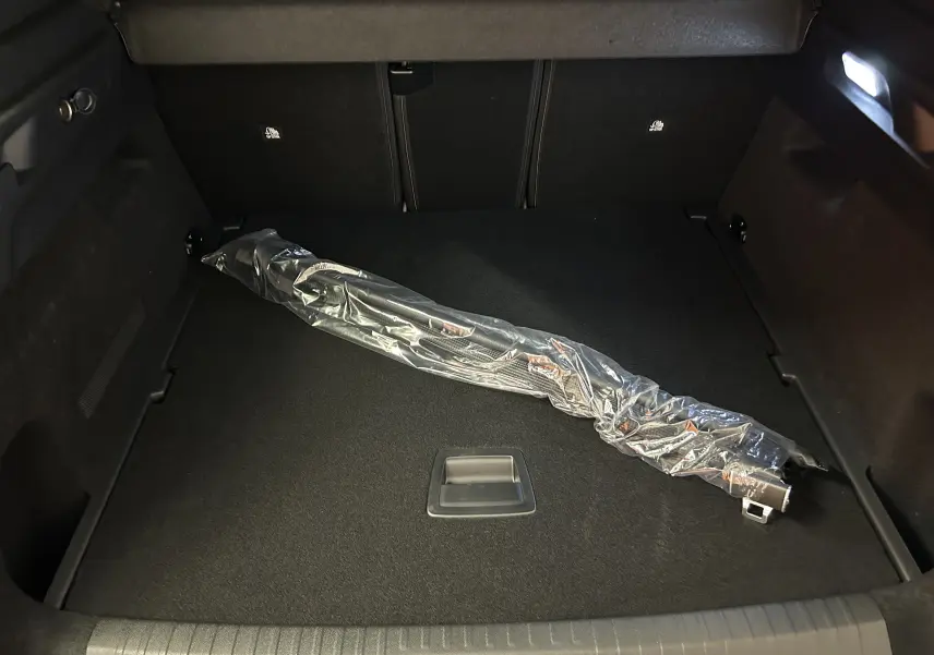 Coffre noir du Peugeot 3008 Hybrid 2026, vue plongeante, avec un accessoire emballé en plastique transparent.