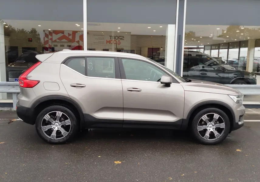 Vue latérale droite d'un Volvo XC40 beige 2020 avec jantes alliage bicolores et protections noires sur les bas de caisse.
