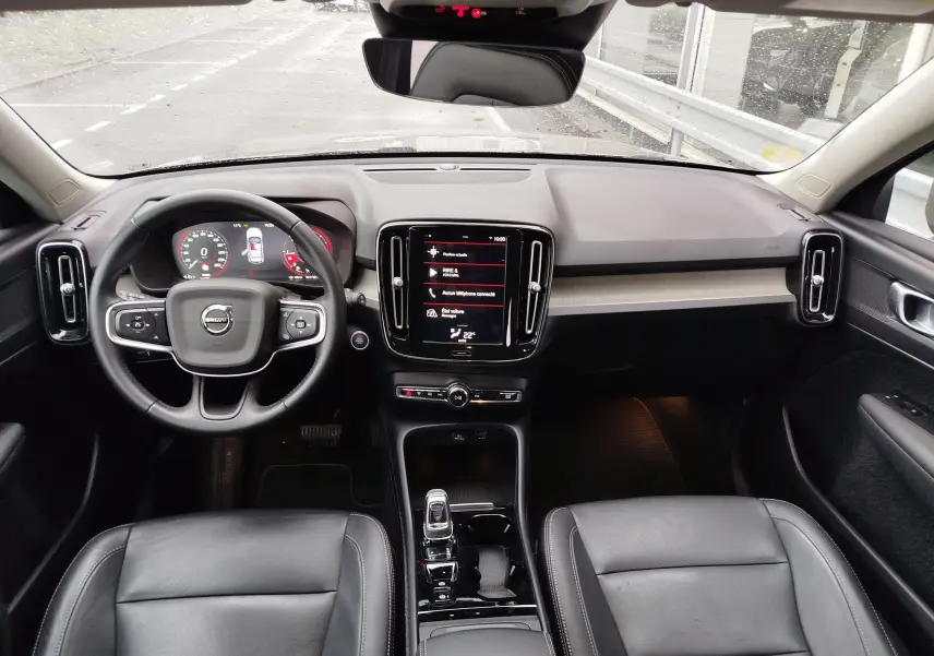 Vue intérieure avant du Volvo XC40 beige 2020, tableau de bord moderne avec écran tactile central et sièges cuir noirs.