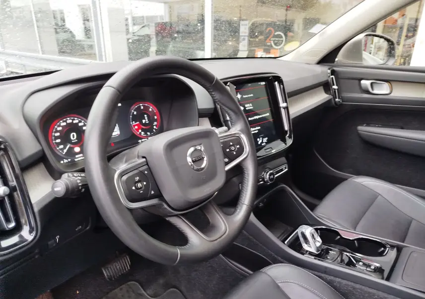 Vue intérieure côté conducteur du Volvo XC40 beige, avec tableau de bord numérique et écran tactile central.